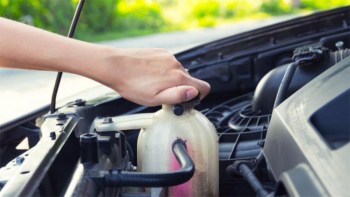 You can see a coolant reservoir in the engine compartment of a car, which contains coolant incl. radiator antifreeze and is currently being opened